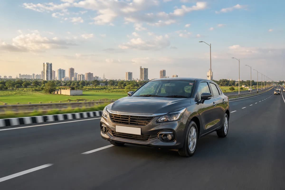 A modern car travelling on a broad Indian highway between farmland and a growing city